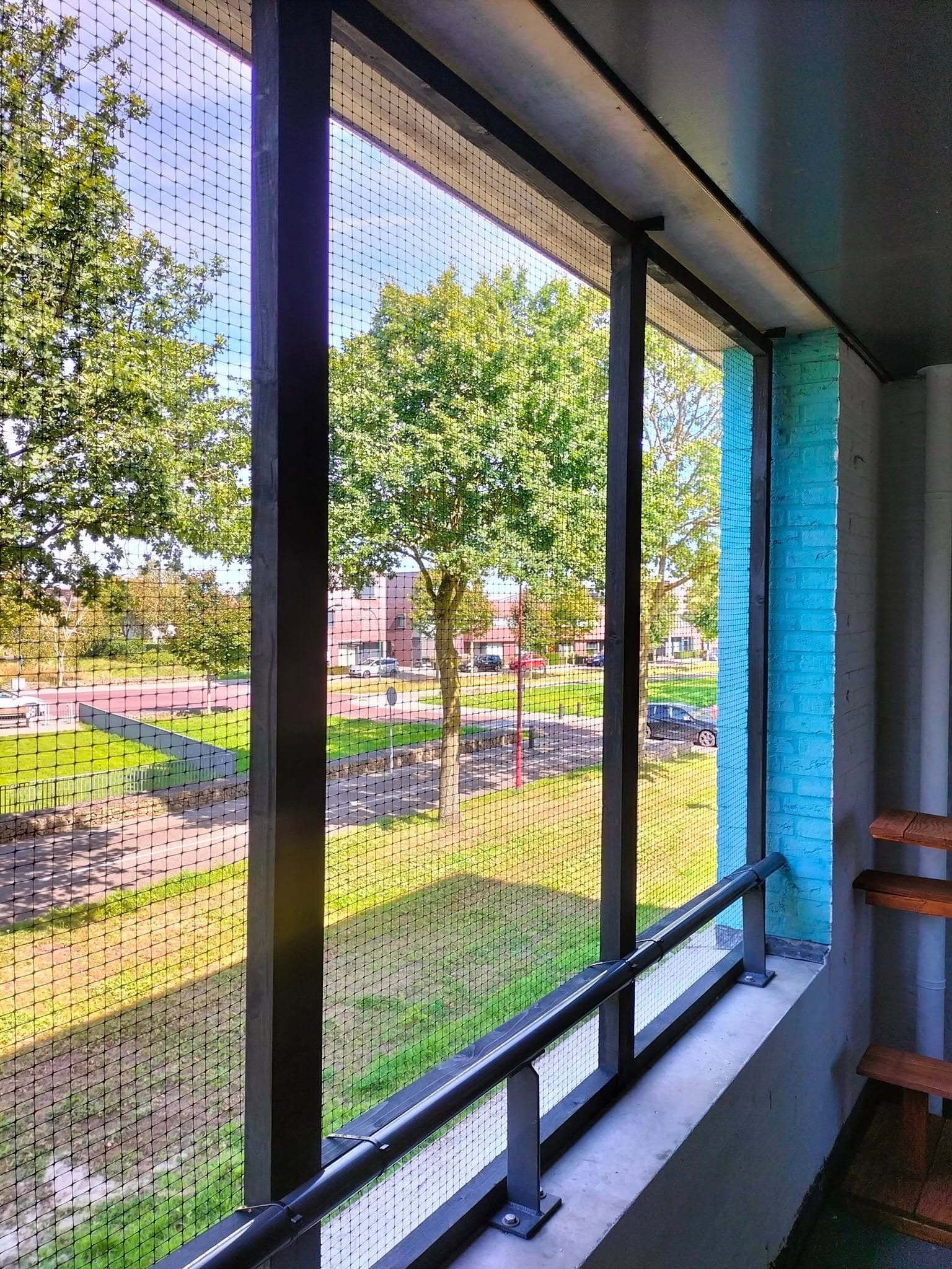 Katzenbalkon mit Netz und einer blau gestrichenen Säule, Blick auf die Straße